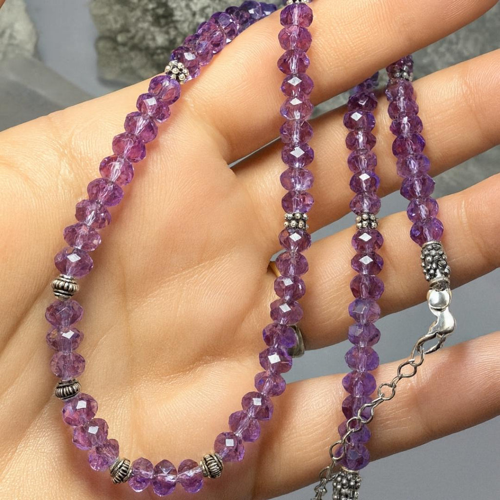 Amethyst bead necklace held in a hand.