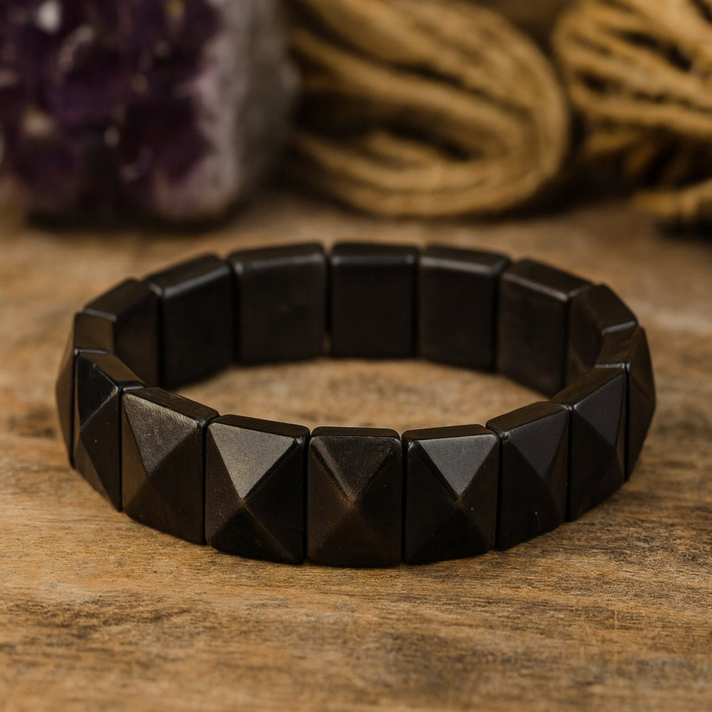Silver Obsidian pyramid bracelet displayed on a warm wooden surface, highlighting its earthy grounding energy. Handcrafted 12x12mm cut stones connected on a flexible elastic band. Natural crystal jewelry for daily wear and spiritual practice. Obsidian protection bracelet, luxury gemstone gift, grounding talisman for men.